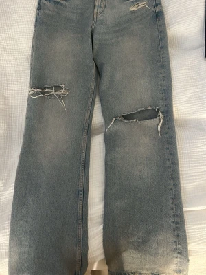 Blå slitna raka jeans med hål - Säljer ett par ljusblå jeans med raka ben och stora slitningar vid knäna. Jeansen kommer från Zara i st 36