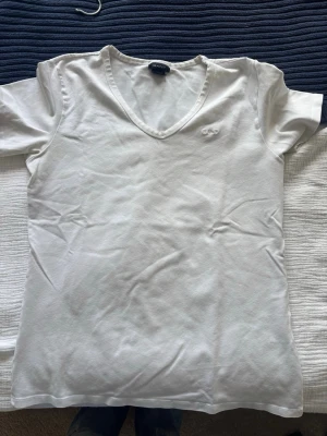 Vit v-ringad t-shirt från GANT - Vit t-shirt från GANT med v-ringad hals och diskret broderad logga på bröstet. Klassisk och enkel design med korta ärmar, perfekt för dig som gillar stilrena plagg. Materialet är mjuk bomull som känns skönt mot huden. Sitter bra på båda S och M så jag vet inte varför de står L