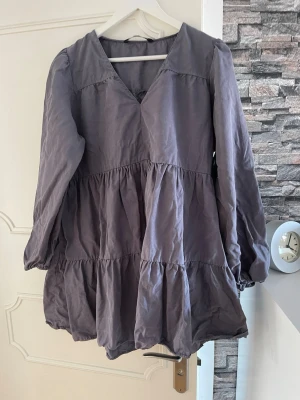 Gråblå volangklänning med v-ringning från Zara i storlek XL - Säljer en gråblå volangklänning med v-ringning och långa ärmar från Zara i storlek XL.. Klänningen har flera volanglager som ger en luftig och avslappnad look. Perfekt för dig som gillar en enkel men ändå trendig stil.