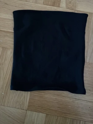 Svart tubtopp från Gina Tricot - En enkel och stilren svart tubtopp från Gina Tricot. Toppen är axelbandslös och har en tight passform som sitter snyggt. 