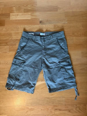 Olivgröna cargoshorts j&j  - Ett prat gröna jättefina gröna cargoshorts från Jack & Jones. Loose passform sitter jättebra och är precis lagom långa. Snöra längst ner för att spänna åt i fall önskas. Knappt använda.