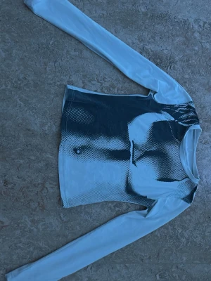 Långärmad topp med grafiskt tryck - Trendig långärmad topp med ett svartvitt grafiskt tryck framtill. Toppen har en tight passform och är tillverkad i ett stretchigt syntetmaterial. 