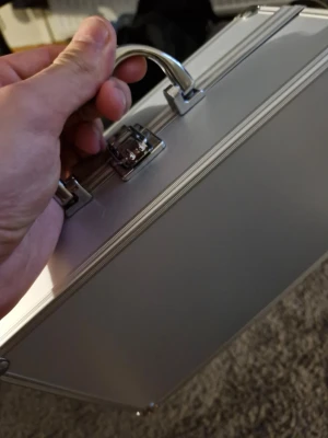 Silverfärgad metallportfölj - Snygg portfölj i silverfärgad metall med robust handtag och två metallspännen. Portföljen har en stilren, rektangulär form och passar perfekt för att bära dokument eller laptop. Enkel och modern design som sticker ut.