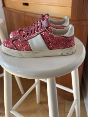 Glittriga rosa sneakers - Säljer ett par riktigt snygga sneakers med rosa glitter och vita detaljer. Skorna har en låg profil och vita sulor. Perfekta för dig som vill sticka ut och addera lite extra bling till din outfit. Materialet är en mix av textil och syntet med glitteryta.Är egentligen storlek 37 men passar bättre om man har 38 då det är stora i storleken. Pris kan diskuteras 