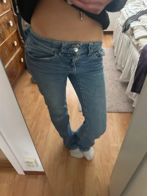 Ljusblå bootcut jeans med låg midja - Säljer ett par ljusblå bootcut jeans med låg midja och klassiska fem fickor. Jeansen har en snygg tvätt och raka ben som går ut lite nedtill. Perfekta för en avslappnad och trendig look.