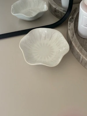 Vit blomformad smyckesskål - Snygg liten smyckesskål i vit keramik med blomformad design och subtilt mönster. Perfekt för att förvara ringar, örhängen eller andra småsmycken på sminkbordet eller nattduksbordet. Enkel och stilren look som passar in i de flesta rum.