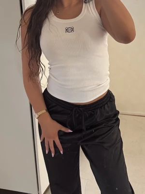 Vit ribbad linnetopp från Loewe - Säljer en vit ribbad linnetopp från Loewe med broderad logga framtill. Toppen är ärmlös och har en tight passform som framhäver figuren. Perfekt att styla med både jeans och kjol för en clean look.