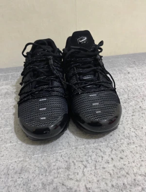 Svarta Nike Air Max sneakers - Snygga svarta Nike Air Max sneakers med mesh-ovandel och reflekterande detaljer. Skorna har en låg profil, klassiska snörningar och en synlig Air-sula för extra komfort. Perfekta för dig som gillar sportig och stilren look.