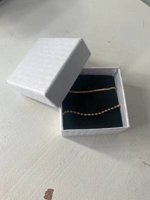 Två tunna guldarmband - Säljer två stilrena armband i guldfärg. Det ena har små runda pärlor längs hela bandet och det andra är en tunn kedja med fyrkantig länk. Båda har justerbar längd och smidiga lås. Perfekta för att kombinera eller bära var för sig.