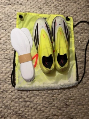 Adidas f50 FG gula fotbollsskor - Säljer ett par Adidas X Speedflow+ FG fotbollsskor i gul och svart med röda detaljer. Skorna har en strömlinjeformad design, ovandel i syntetmaterial och levereras med extra innersulor och en praktisk skopåse. Perfekta för snabba spelare på naturgräs.