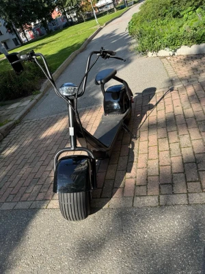 Svart elscooter med breda däck - Säljer en svart elscooter med breda däck och hög styre. Scootern har en stor sits, fotplatta och handtag med metall- och gummidetaljer. Utrustad med framlampa och bromshandtag. Perfekt för smidig transport i stan. Har använt den max 5 gåmger. Den kan köra runt 55 kmh och har räckvid på 30 km. Köp bara vid upphämtning vid Jakobsberg centrum 