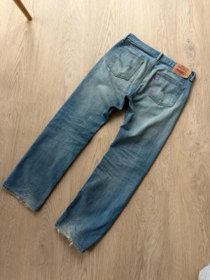 Levi's vintage 501 - Klassiska vintage blå Levi's 501 jeans med rak passform och slitna detaljer vid bensluten. Jeansen har fem fickor, läderpatch bak i midjan och är tillverkade i bomullsdenim med snygg tvättad look.