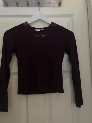 Vinröd långärmad topp med spets - Snygg vinröd långärmad topp med v-ringning och dekorativ spetsdetalj runt hals. 