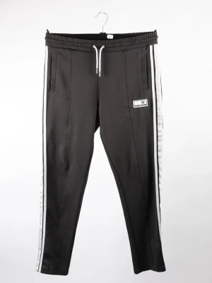 Svarta mjukisbyxor från Sergio Tacchini - Snygga svarta mjukisbyxor från Sergio Tacchini med vita sidoränder och dragsko i midjan. Byxorna har två fickor fram och en bakficka samt en liten logga på vänster ben. Tillverkade i ett mjukt och stretchigt material som känns skönt mot huden.