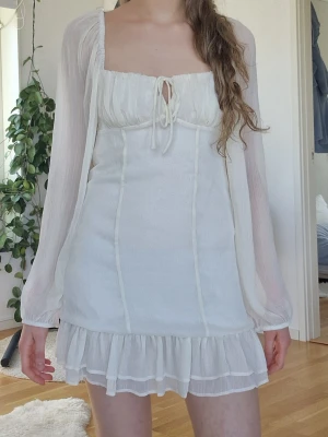 Vit kort klänning med volang - Söt vit kortklänning med långa, transparenta ärmar och volangkant nedtill.                                        Perfekt till studenten och sommaren! 💛  Den är vit/creme färgad