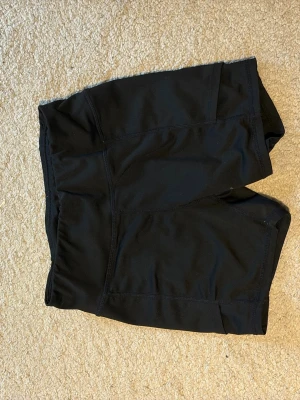 Svarta träningstights shorts - Svarta shorts i stretchigt material från Virtus, perfekta för träning. De har en tight passform och hög midja för extra komfort. Snygg och enkel design med liten logga bak. Passar dig som vill ha funktionella och stilrena träningsshorts.