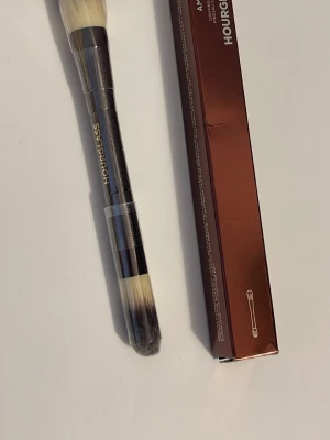 Hourglass dubbelsidig sminkborste - Snygg dubbelsidig sminkborste från Hourglass med svart och metallfärgat handtag. Borsten har täta, syntetiska strån i vit och svart ombre. Perfekt för applicering och blending av smink. Kommer i originalförpackning i kopparfärg.