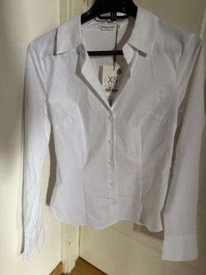 Vit klassisk skjorta från Stradivarius - Säljer en stilren vit skjorta från Stradivarius i figurnära modell. Skjortan har långa ärmar, klassisk krage och knappar framtill. Tillverkad i mjuk bomull som känns skön mot huden. Perfekt att styla till jeans eller kjol för en clean look.