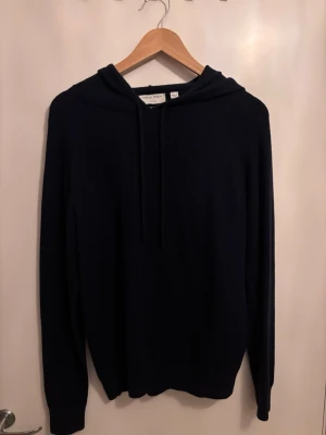 Mörkblå Tiger of sweden hoodie - Mysig mörkblå hoodie från Tiger of Sweden i mjuk och lyxig kashmir. Klassisk modell med huva och dragsko, samt långa ärmar. Perfekt för dig som gillar stilrena och bekväma plagg med premiumkänsla.