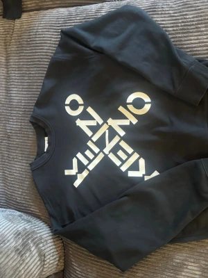 Svart Kenzo sweatshirt med tryck - Cool svart sweatshirt från Kenzo med stort vitt tryck på framsidan och litet tryck vid nacken på baksidan. Tröjan har rund halsringning och långa ärmar. Perfekt för dig som gillar streetwear och vill sticka ut med en snygg logga. Lite oversized modell. Pris ej fast!