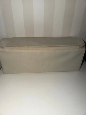 Beige avlång förvaringsväska i tyg IKEA Kloptil - Säljer en beige, avlång förvaringsväska i tyg med dragkedja. Perfekt för att organisera småprylar eller accessoarer. Enkel och stilren design utan synligt märke. Väskan har en mjuk struktur och neutralt utseende som passar in i de flesta rum., mått B 15 cm, L 40 cm, H 14 cm.