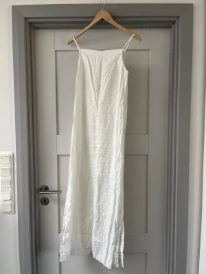 Vit långklänning i linne - Säljer en stilren vit långklänning med smala axelband . Perfekt för sommarens alla tillfällen.