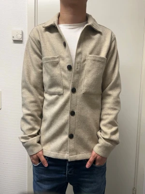 Jack & Jones overshirt - Snygg beige overshirt från Jack & Jones. Väldigt bra skick. Materialet är 92% polyester, 8% viskos. Modellen är 173cm, 64kg. Pris kan diskuteras!!