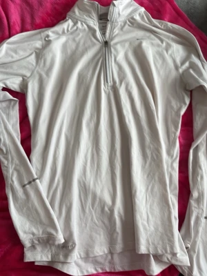 Vit långärmad träningströja Nike - Säljer en vit långärmad träningströja från Nike med halv dragkedja och Dri-FIT-material som andas. Perfekt för löpning eller gym. Tröjan har diskret Nike-logga på bröstet och tumhål vid ärmsluten för extra komfort. Fick den av mormor och har aldrig använt!
