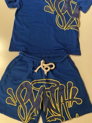 Syna World set (T-shirt och shorts) i blått  - Snyggt Syna wrld set i blått med blå gul text. Helt oanvänt. Storlek M               Pris kan sänkas   Kan skickas mer bilder om man vill se mer.