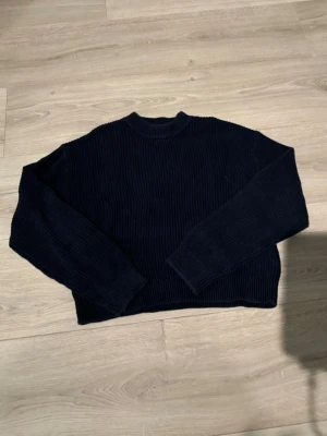 Svart ribbstickad tröja - En svart ribbstickad tröja med rund hals och långa ärmar. Tröjan har en croppad passform och är tillverkad i ett tjockare stickat material som ger en mysig känsla. Perfekt för kyligare dagar och enkel att matcha med olika outfits.