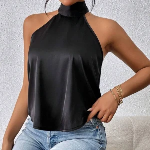 Svart halterneck topp med knytband - Säljer en svart halterneck topp i glansigt satinliknande material. Toppen har hög hals, ärmlös design och öppen rygg med breda knytband i nacken. Perfekt för dig som gillar en stilren och trendig look. Passar snyggt till jeans eller kjol.
