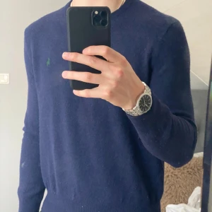 Mörkblå tröja från Polo Ralph Lauren - Säljer en stilren mörkblå tröja från Polo Ralph Lauren med broderad grön logotyp på bröstet. Tröjan har en klassisk design med rund hals och långa ärmar. Perfekt för kyligare dagar men passar nästan alla tillfällen😊
