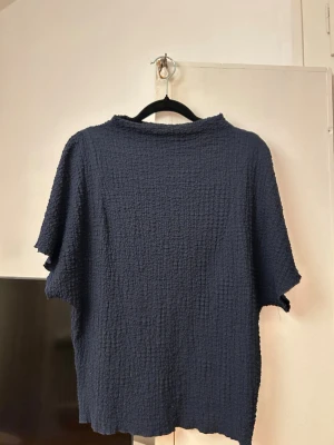 Mörkblå topp från Zara - Säljer en mörkblå topp från Zara med korta ärmar och en loose passform. Tyget är strukturerat och ger en cool, avslappnad vibe. Perfekt till jeans eller kjol för en enkel men snygg look.