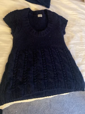 Mörkblå stickad topp från Oasis - Mörkblå stickad topp från Oasis med korta ärmar och bred ribbad halsringning. Tröjan har ett snyggt kabelstickat mönster och är gjord i ett mjukt material som passar perfekt till lager på lager. Enkel att styla till både jeans och kjol.