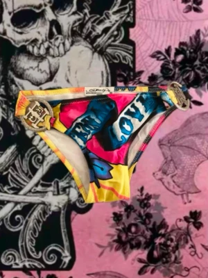 Färgglada bikiniunderdel från Ed Hardy - ❗️OANVÄNDA❗️Snygg bikiniunderdel från Ed Hardy med färgstarkt tryck i gult, rosa, blått och svart. Har coola metalldetaljer i guld på sidorna och textmotiv. Perfekt för dig som vill sticka ut på stranden! Ed Hardy loggan är på baksidan! Köpta för 500 kr! ❗️PRIS KAN DISKUTERAS❗️