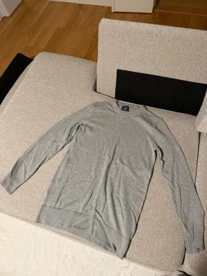 Grå tröja från H&M - Snygg grå långärmad tröja från H&M i slim fit-modell. Tillverkad i mjukt material med ribbade muddar vid hals, ärmslut och nederkant. Enkel och stilren design som passar perfekt till jeans eller chinos.