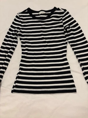 Randig långärmad topp Gina Tricot - Säljer en svartvit långärmad topp från Gina Tricot i modellen Basically Basic. Toppen har smala horisontella ränder och är gjord i mjuk ribbad bomull. Perfekt till jeans eller kjol för en enkel och stilren look.