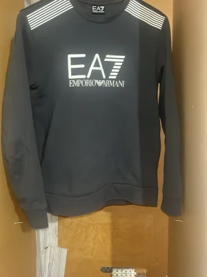 Svart sweatshirt EA7 Emporio Armani - Svart sweatshirt från EA7 Emporio armani tröjan är i väldigt bra skick och har bara använts ett få antal gånger. Om du inte är nöjd med det satta priset så kan vi självklart förhandla .