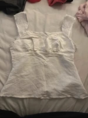 Vit linnetopp med breda axelband - Säljer en söt vit linnetopp med breda axelband och lätt v-ringad urringning. Toppen har en figurnära passform och är tillverkad i ett luftigt linnematerial, perfekt för varma dagar. Enkel och stilren design som passar till mycket.