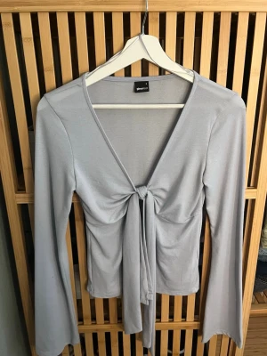 Ljusblå långärmad topp med knyt - Trendig ljusblå långärmad topp från Gina Tricot med v-ringning och snygg knytning framtill. Tillverkad i mjukt och stretchigt material som sitter skönt på kroppen. Perfekt för att skapa en stilren och modern look.