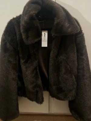 Mörkbrun fuskpälsjacka Gina Tricot - Säljer en fluffig och lyxig mörkbrun fuskpälsjacka från Gina Tricot. Jackan har bred krage, långa ärmar och en mjuk, glansig finish. Perfekt för dig som vill ha en trendig och varm look under vintern. Stängs framtill och har en klassisk, rak passform.