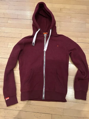 Vinröd hoodie från Superdry - Säljer en vinröd hoodie från Superdry med dragkedja. Hoodien är i storlek M. Va inte rädd för att ställa frågor!!