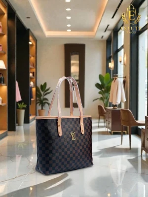 Louis Vuitton brun handväska - Stilren handväska från Louis Vuitton i brunt med klassiskt rutigt och monogrammönster. Väskan har långa ljusbeiga handtag och guldiga detaljer. Tillverkad i canvas med läderdetaljer, perfekt för dig som vill ha en ikonisk och rymlig väska.