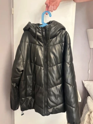 Svart pufferjacka med huva - Säljer en svart pufferjacka från pull&bear i glansigt ”läder” liknande material med dragkedja framtill och stor luva med dragsko💕 Väldigt sparsamt använd och superfint skick! 