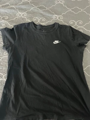 Svart Nike t-shirt med logga - Klassisk svart t-shirt från Nike med vit logga på bröstet. T-shirten har rund halsringning och korta ärmar. Tillverkad i mjuk bomull för en skön och avslappnad look.