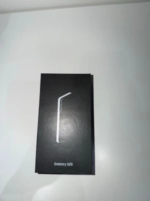 Samsung Galaxy S25 svart kartong - Säljer en Samsung Galaxy S25 i original svart kartong. Lådan har en stilren design med vit logotyp och text. Perfekt för dig som vill ha en modern Android-telefon från Samsung med snygg och minimalistisk förpackning.