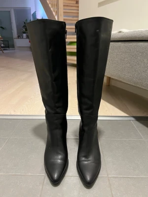 Svarta knähöga boots med klack - Novita Snygga svarta knähöga stövlar i slätt skinnimitation med spetsig tå och blockklack. Dragkedja på insidan för enkel påtagning. Perfekta för att lyfta din outfit med en stilren och trendig look. been used only two times. waterproofed.