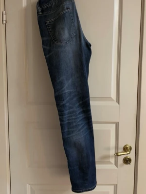 Blå jeans från American Eagle - Snygga blå jeans från American Eagle med halv slitningar framtill. Jeansen har en slim passform och är tillverkade i ett mjukt denimtyg som ger en bekväm känsla. 