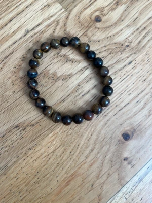 Armband med bruna tigeröga pärlor - Snyggt armband med runda pärlor av tigeröga i bruna och gyllene toner. Elastisk tråd gör det enkelt att ta på och av. Perfekt accessoar för dig som gillar naturliga stenar och en jordnära look.
