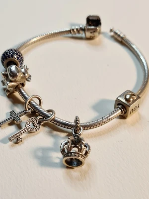 Pandora armband med berlocker Bl.a "I love you cube" "Pave light blue" o - Så fint Pandora Snake Länk armband med 6 stycken fina berlocker, bland annat "I love you cube" sterling silver och hjärta 14K guld, pave lights blue och Noble Splendor Crown. Armbandet mäter ca 18 cm och är använt men i fint skick (se bilder). Perfekt för Valentine! 